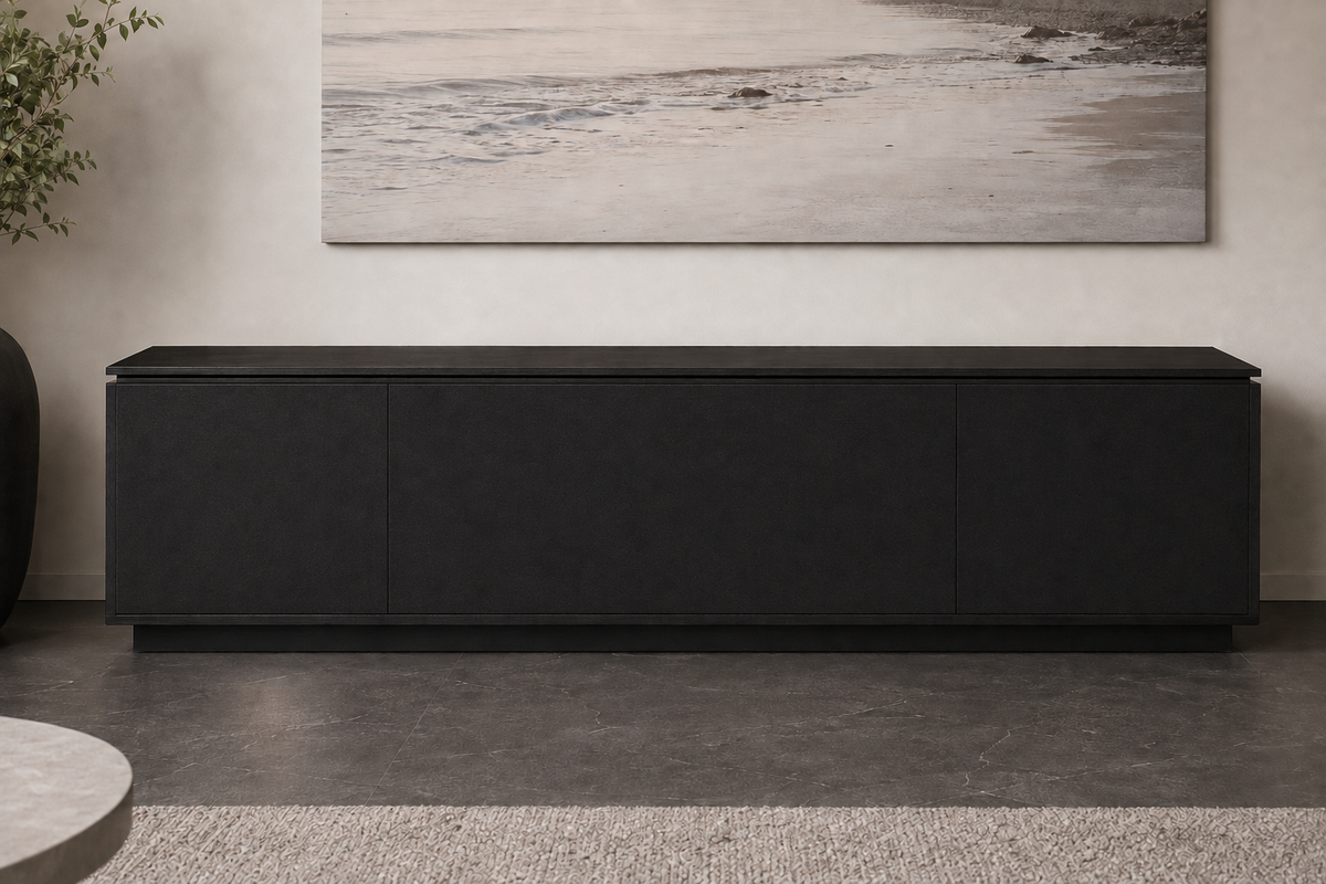 A long, low black sideboard or credenza with three front doors, shown in a modern interior setting with a textured gray floor, a beige wall, a large landscape painting, and a small plant.